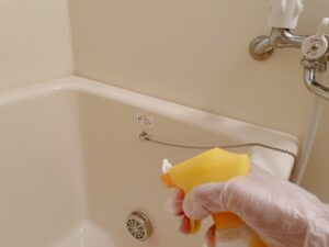 手袋をした手で浴槽まわりに洗剤をかけるところ
