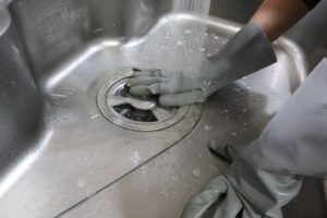 手袋をしてステンレスシンクの排水口を洗うところ