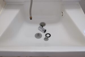 白い防水パンの上に並べた排水トラップの部品と排水ホース